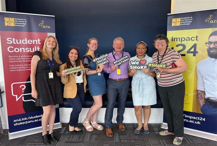 Photograph of the SHoKE delivery team and students holding signs that say #Positive social impact and we love SHoKE