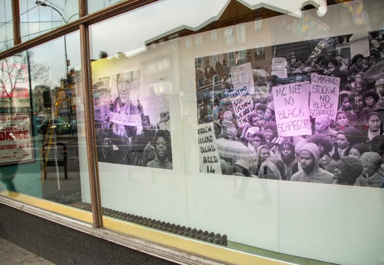 Pop up exhibition at Catford Broadway commemorating the Black Peoples' Day of Action 1981. Photo of two photos within a shop window of people with placards.