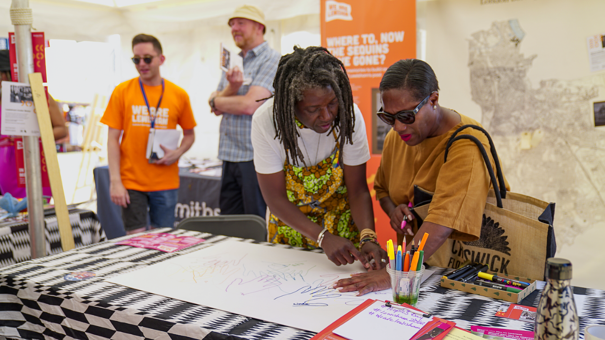 Photo of two people undertaking an In Living Memory activity at a stall at Lewisham People's day (drawing around their hands onto a sheet of paper).