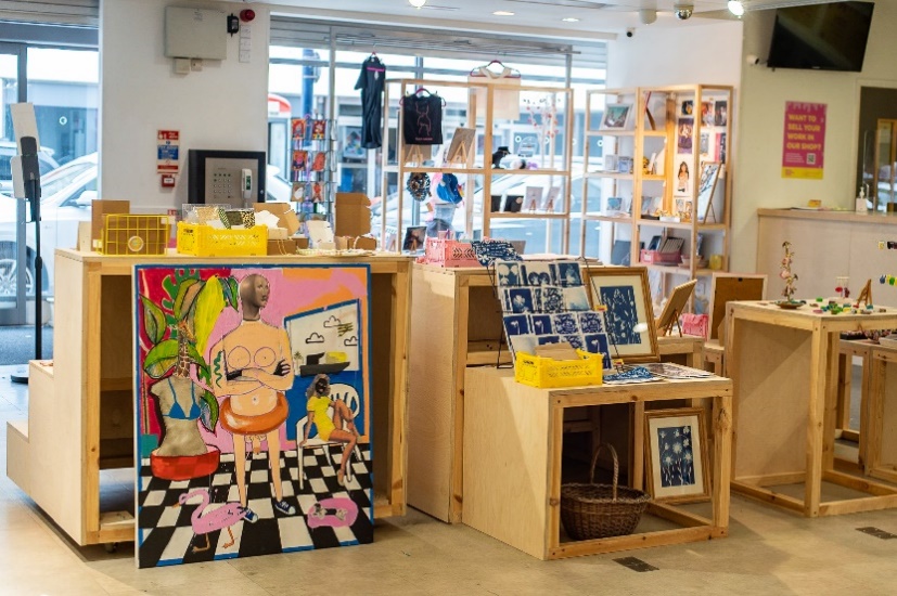 A display of brightly coloured, modern artworks and crafts including a large painting, postcards of cyanotype prints of flowers, and jewellery.