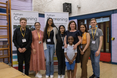 Group of seven young people and one child all smiling located in a school hall