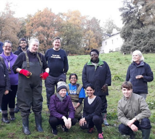Group of ten people smiling wearing outdoor clothing in a large grass space.