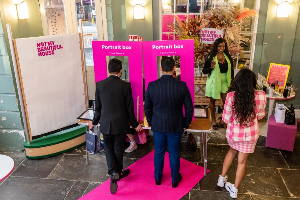 Small group of people interacting with brightly coloured exhibits, including a 'portrait box' in the entrance of the Market House