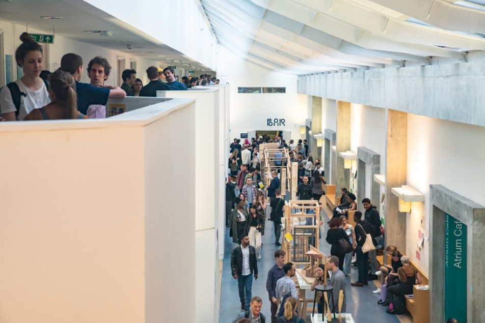 The Summer Show at our Aldgate campus. The image shows crowds of people on split levels chatting and view art objects.