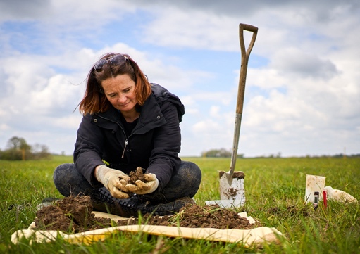 MScR student Yolande sat in a field with a trowel conducting research