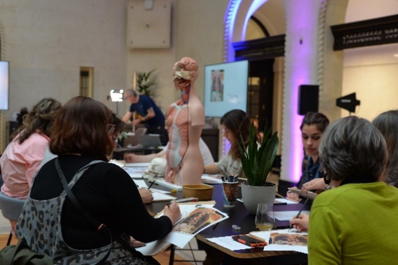A picture taken inside The Exchange, showing six people sat around a table, which has an anatomical model of a human in the middle. The participants have paper in front of them, which they are annotating.