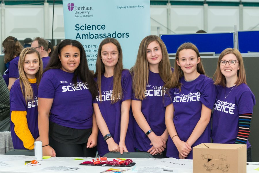 Six young women in purple t-shirts beside a banner that reads 'Science Ambassadors'.