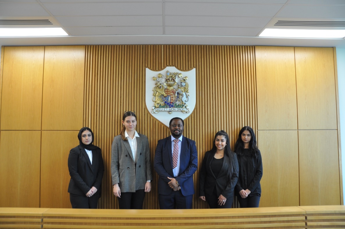 Photohraph of a group of people standing in front of a wood paneled wall in the Law department court room