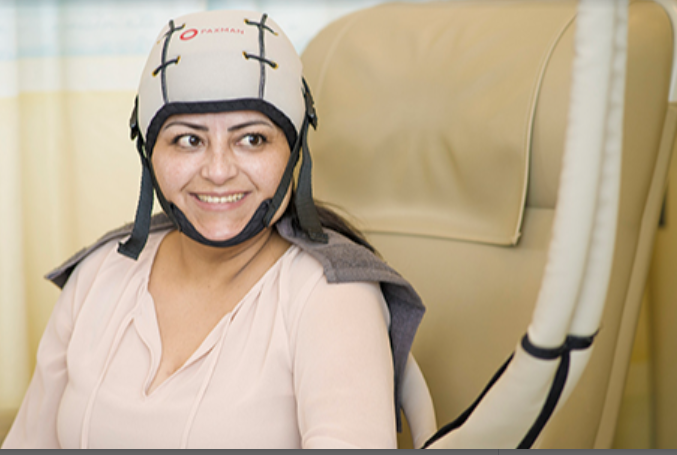 A smiling woman sits on an armchair and wears a Paxman Cooler on her head