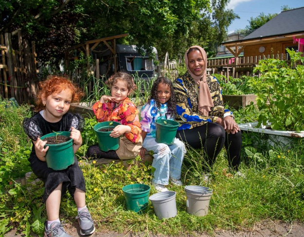 A woman and three children holding plant pots in a garden