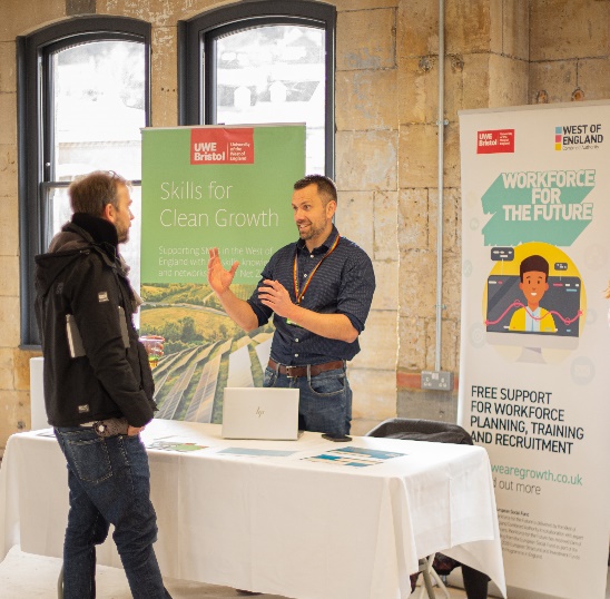 Two people standing next to a table with a sign at a conference event