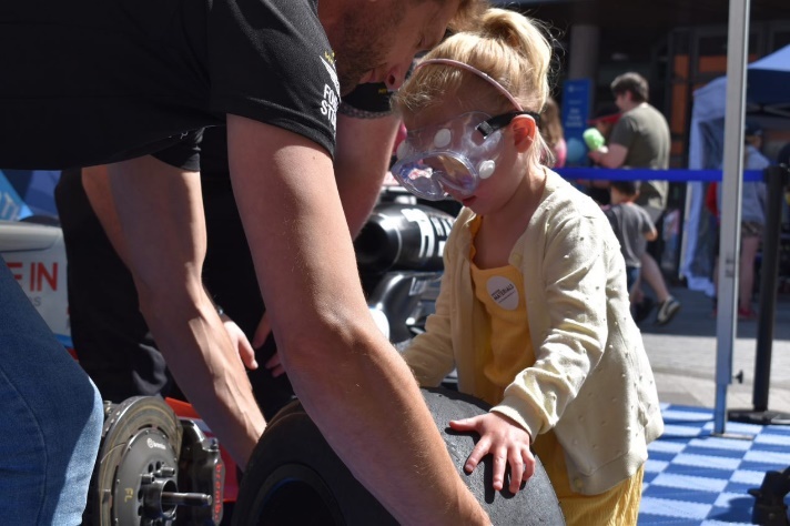 Photograph of young girl being helped to change a trye on the UWR racing car