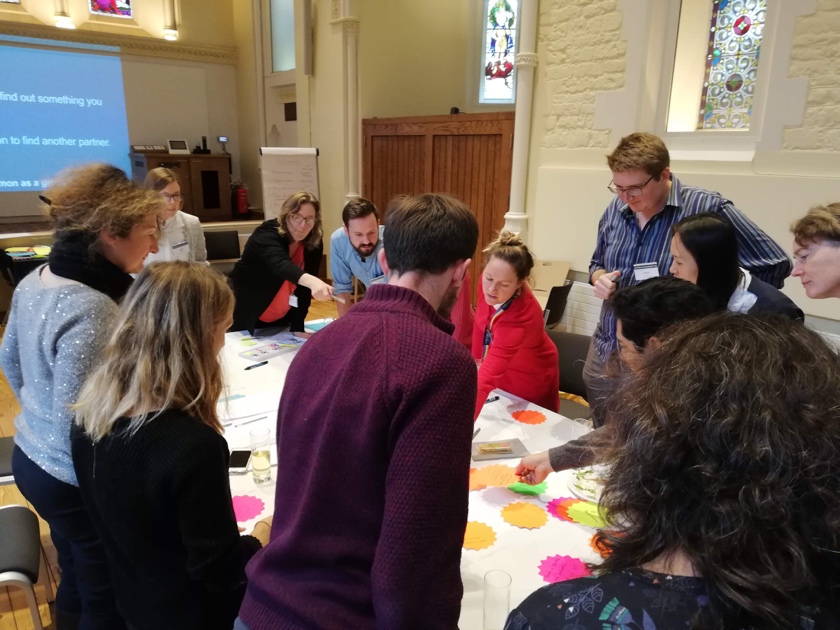A group of people standing around a table placing colourful sticky notes on flip-chart paper
