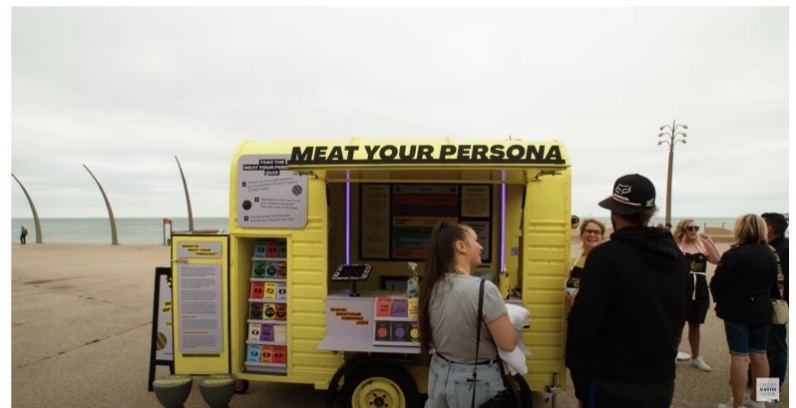 Screenshot of Youtube video featuring the Meat Your Persona: the National Tour, with a image of people standing around the Meat Your Persona yellow cart on a beach front.