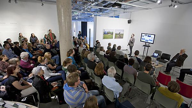 A room full of people sat in rows listening to a panel discussion at the front of the room. Hosted at the University of Plymouth's Art Institute.