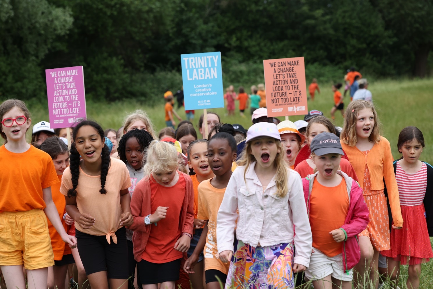 Picture of a group of children marching and chanting in a park. They hold placards calling for climate justice.